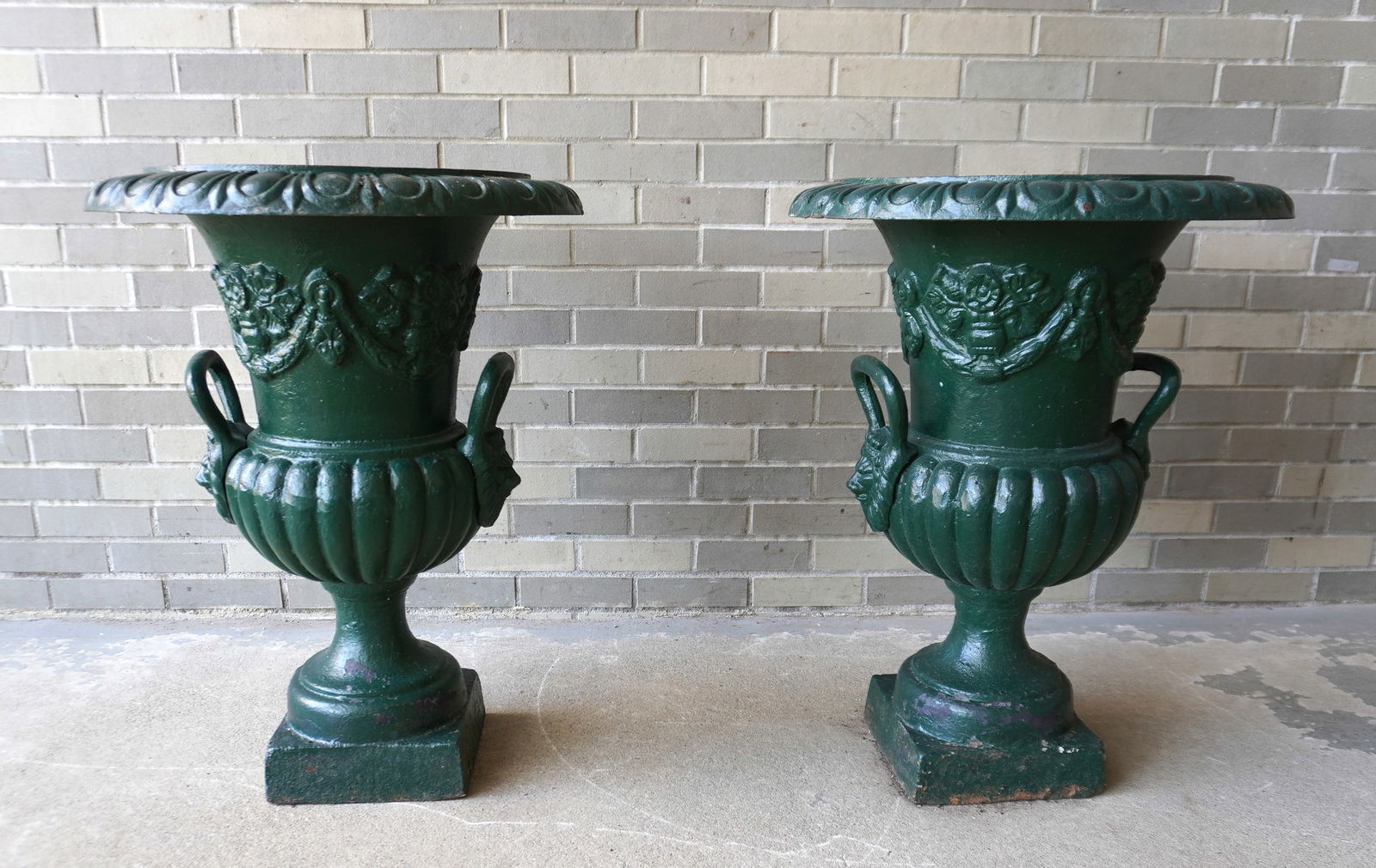 A matched pair of cast iron garden urns mounted on pedestal bases, in green paint. Early to mid 20th