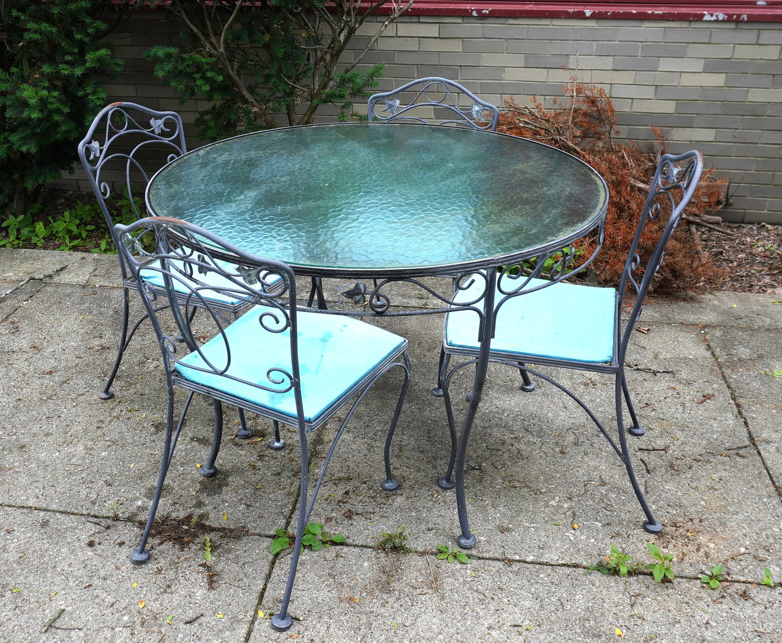 A quality wrought iron patio set consisting of a glass top table and 4 matching chairs, probably: A quality wrought iron patio set consisting of a glass top table and 4 matching chairs, probably Woodard. The table with tempered glass top, measures 48" diameter x 29"H and the chairs 20 1/2"W x 23"D