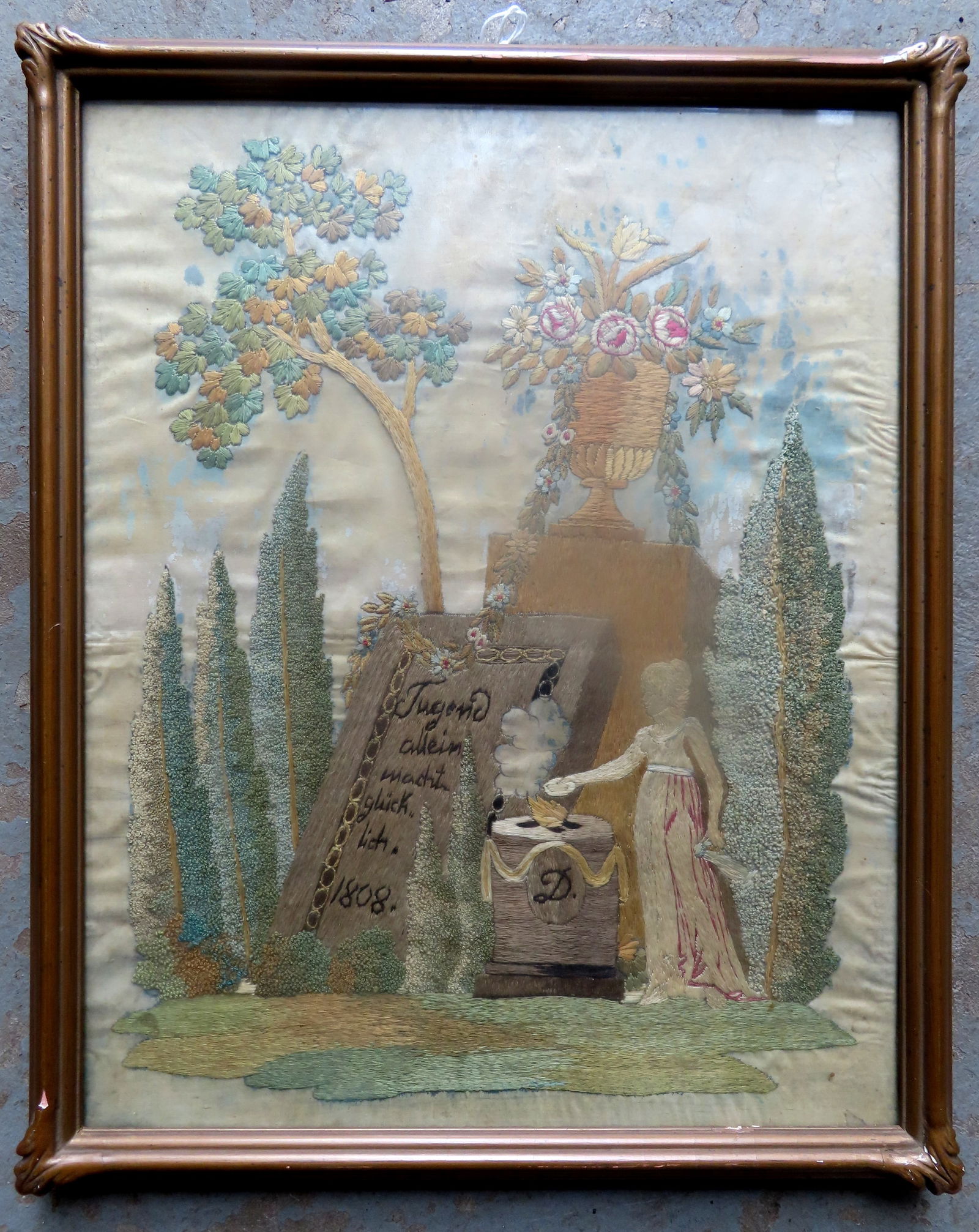 A very detailed mourning silk embroidery, with German inscription and dated 1808. Appears to be: A very detailed mourning silk embroidery, with German inscription and dated 1808. Appears to be housed in original gilt frame with decorated corners. Some bleeding from the colors of threads into silk