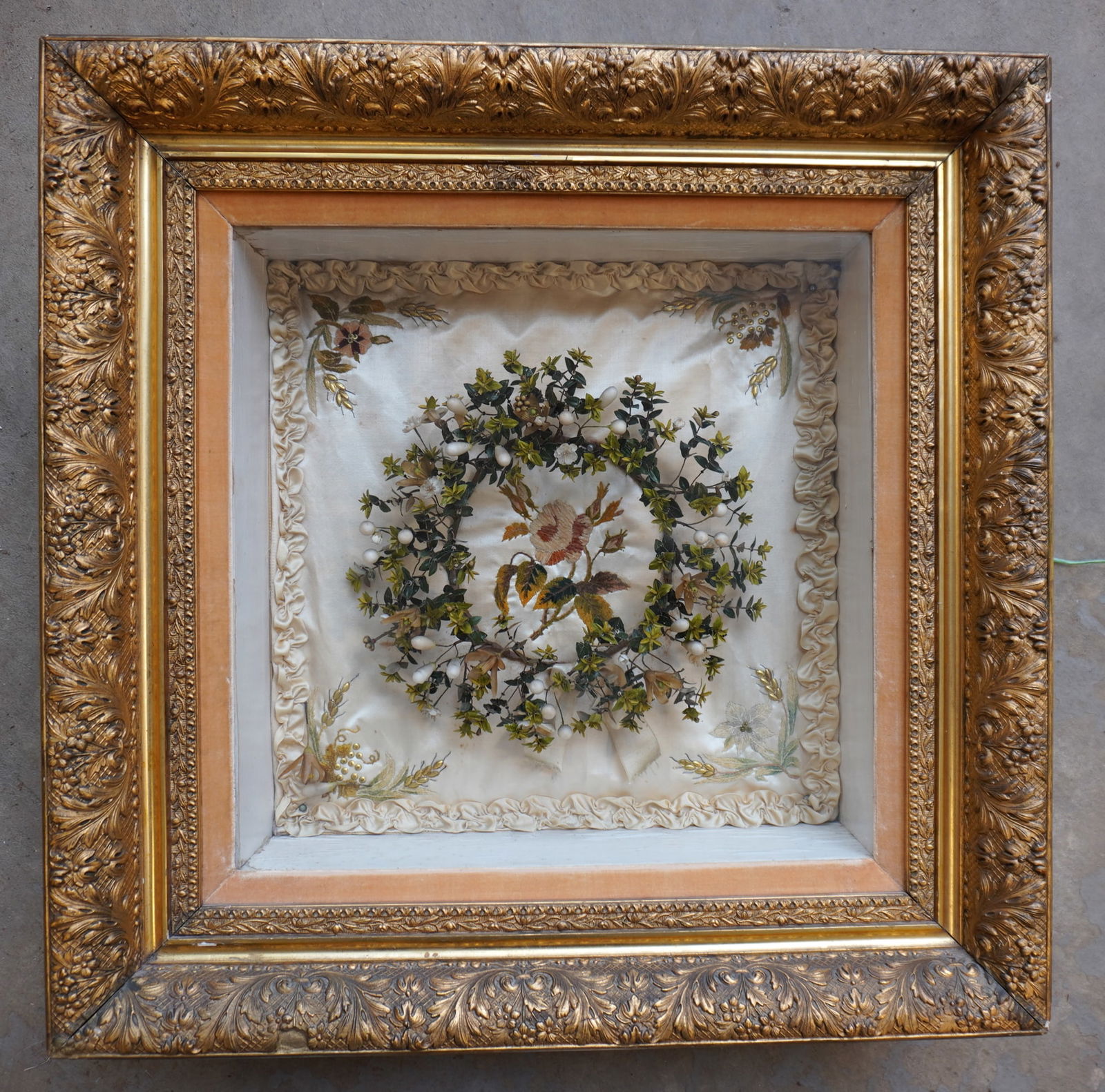 A Victorian wreath decorated with hand made flowers, leaves and berries, housed in its original gilt: A Victorian wreath decorated with hand made flowers, leaves and berries, housed in its original gilt gesso shadowbox frame decorated with leaves and flowers. The wreath against a silk embroidered back