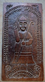 An early carved wooden plaque of a bishop pointing to heaven having a carved vine and floral border,