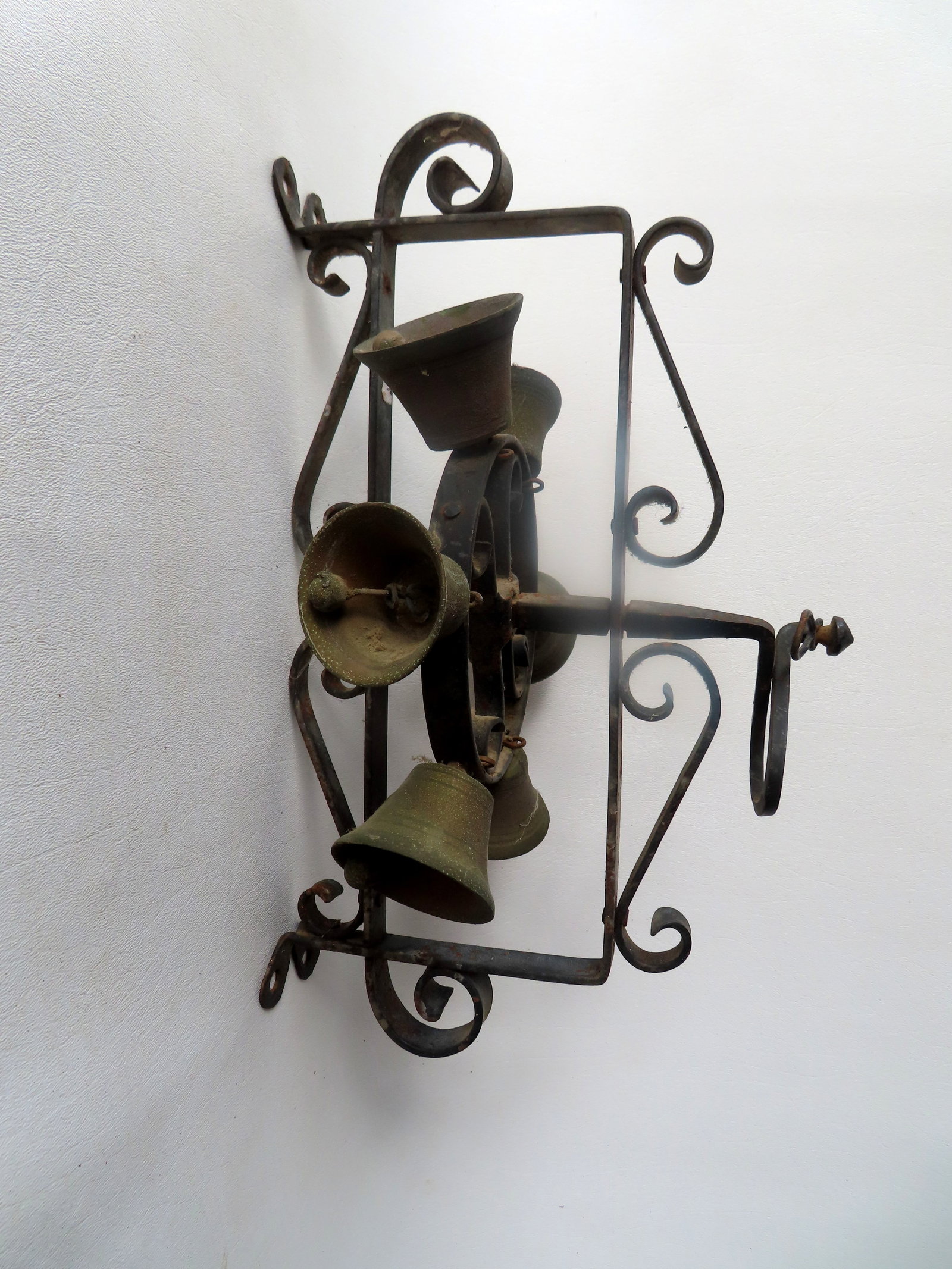 A wall mounted revolving wrought iron farmhouse bell decorated with applied scrolls and with 6 brass: A wall mounted revolving wrought iron farmhouse bell decorated with applied scrolls and with 6 brass bells mount on a circular iron strap with handle that allows the bells to ring when turned, late 19