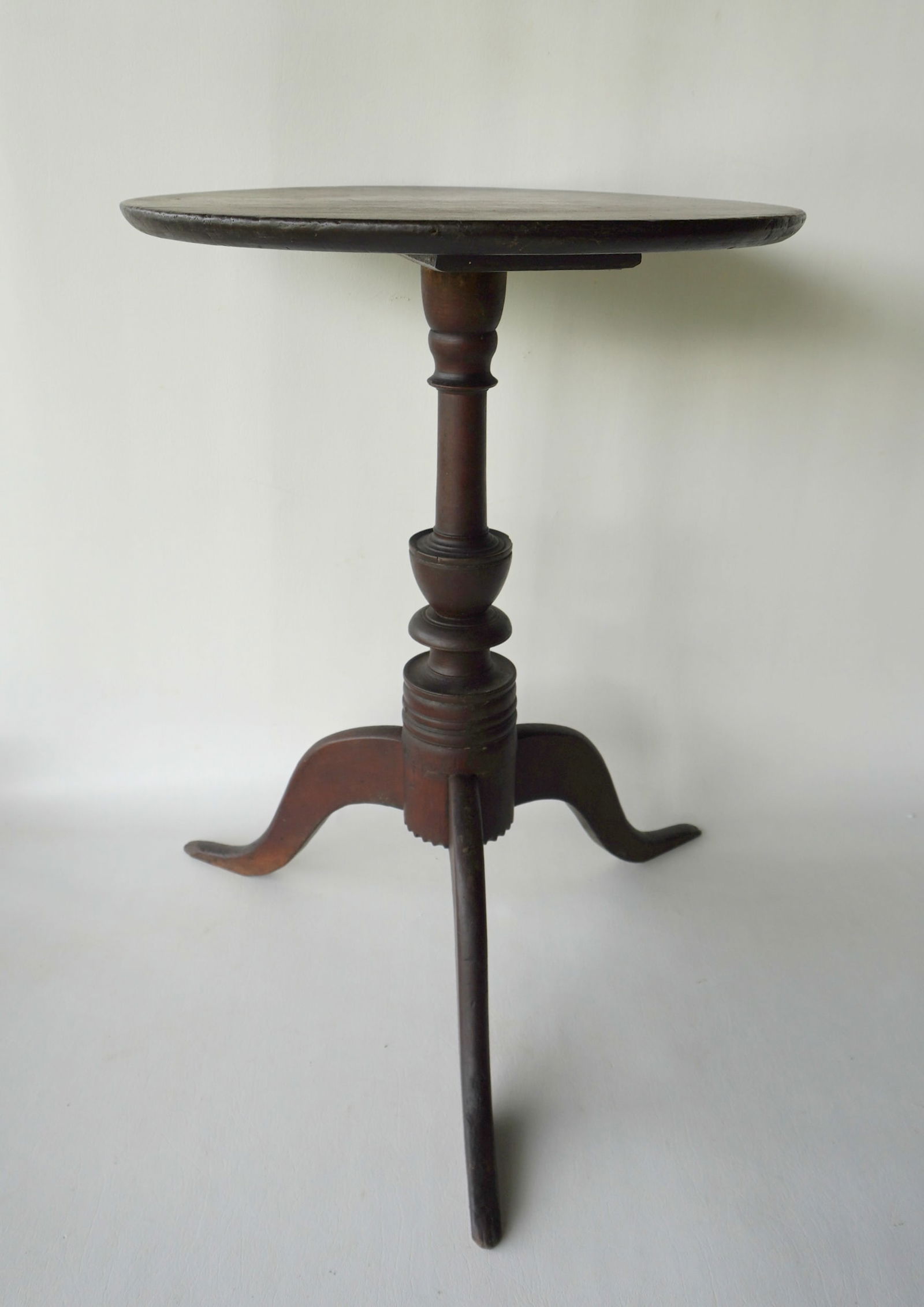 A good New England candlestand with round top, elaborately turned column having an urn over other: A good New England candlestand with round top, elaborately turned column having an urn over other turnings leading to snake feet, circa 1800. Darkened finish, either cherry or walnut, good structural