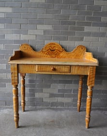 A mustard colored grain painted work table with center drawer and shaped backsplash with stylized