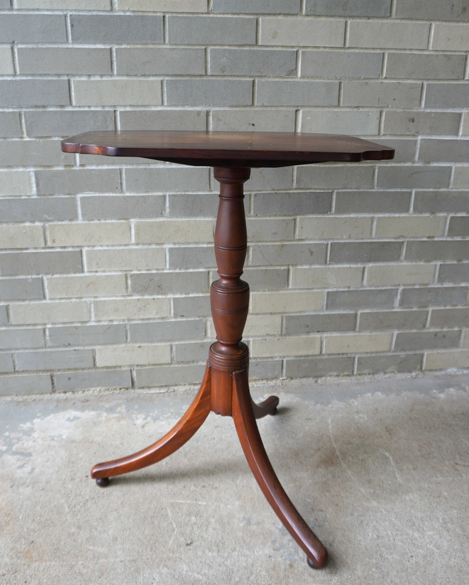 An early butternut tilt top candlestand with shaped top, and 3 legs with ball feet extending from: An early butternut tilt top candlestand with shaped top, and 3 legs with ball feet extending from turned column. The top with stained center that likely held a vase, otherwise very good condition. Mea