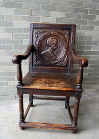 A Jacobean style religious chair with a carved saint on the back and having rolled arms and turned
