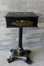 A paper mache black lacquered sewing stand decorated with gilded scrolls and flowers and having a