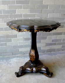 A fancy black lacquered and gilded Victorian game table with shaped top, mounted on pedestal base