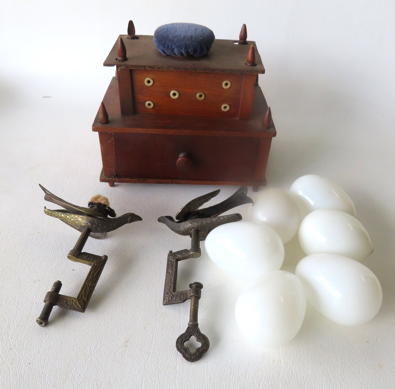 Grouping of vintage sewing related articles including: A 2 tier Shaker sewing box with pincushion: Grouping of vintage sewing related articles including: A 2 tier Shaker sewing box with pincushion and lower drawer; 2 sewing birds, both with patent date 1856; and 6 hand blown milk glass darning eggs