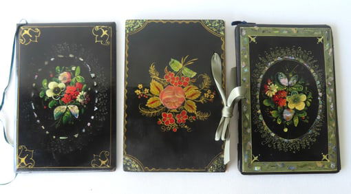Three hand painted black lacquered book covers decorated with flowers, one used as a photo case, all