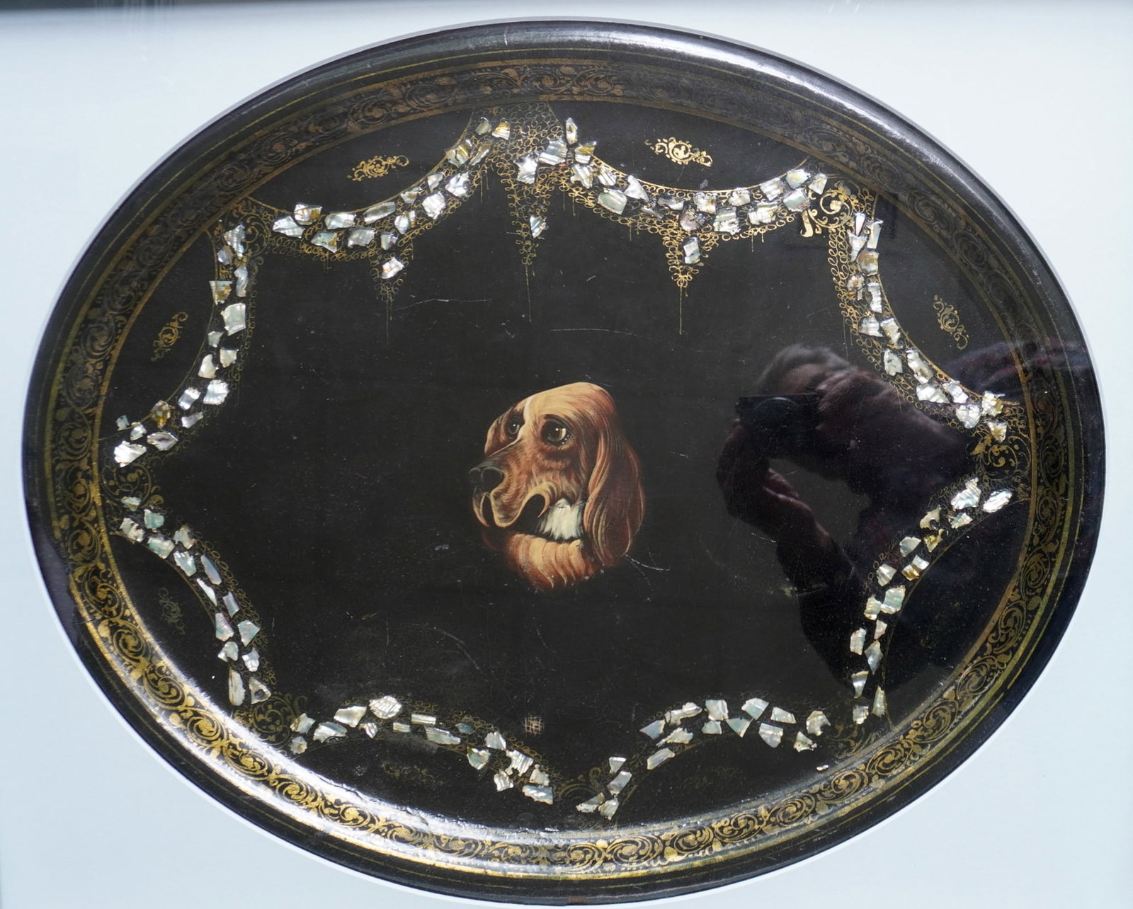 A framed black lacquered toleware tray with gilded scrolls decorating the boarder and having mother: A framed black lacquered toleware tray with gilded scrolls decorating the boarder and having mother of pearl swags surrounding a hand painted portrait of a dog. Circa 1960-80; Very good condition, pro
