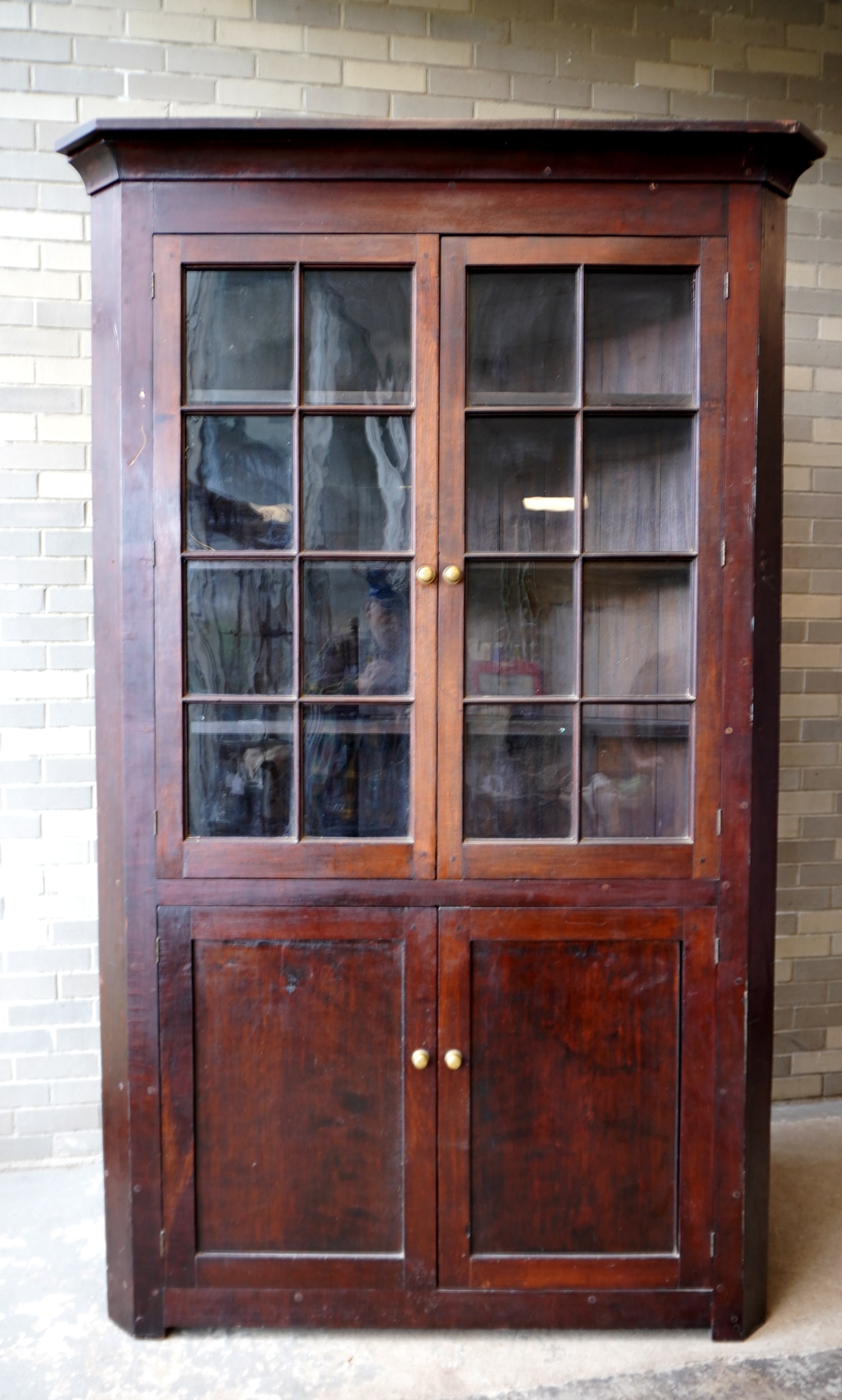 A cherry 1 piece corner cupboard having 2 glass doors each with 8 glazed lights over 2 solid doors,: A cherry 1 piece corner cupboard having 2 glass doors each with 8 glazed lights over 2 solid doors, with plate rails and mounted on cutout base in original darkened finish - cornice is also original,