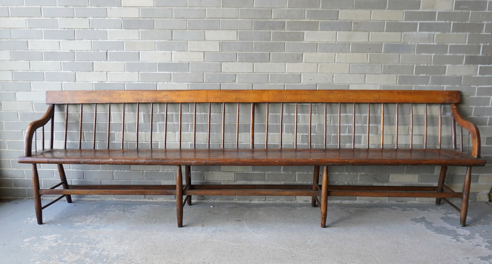 A long country spindle back meeting house bench, old finish, plank seat, traces of old green paint,: A long country spindle back meeting house bench, old finish, plank seat, traces of old green paint, shaped arms and mounted on turned legs with stretchers, circa 1820-40. Some use wear, but overall go