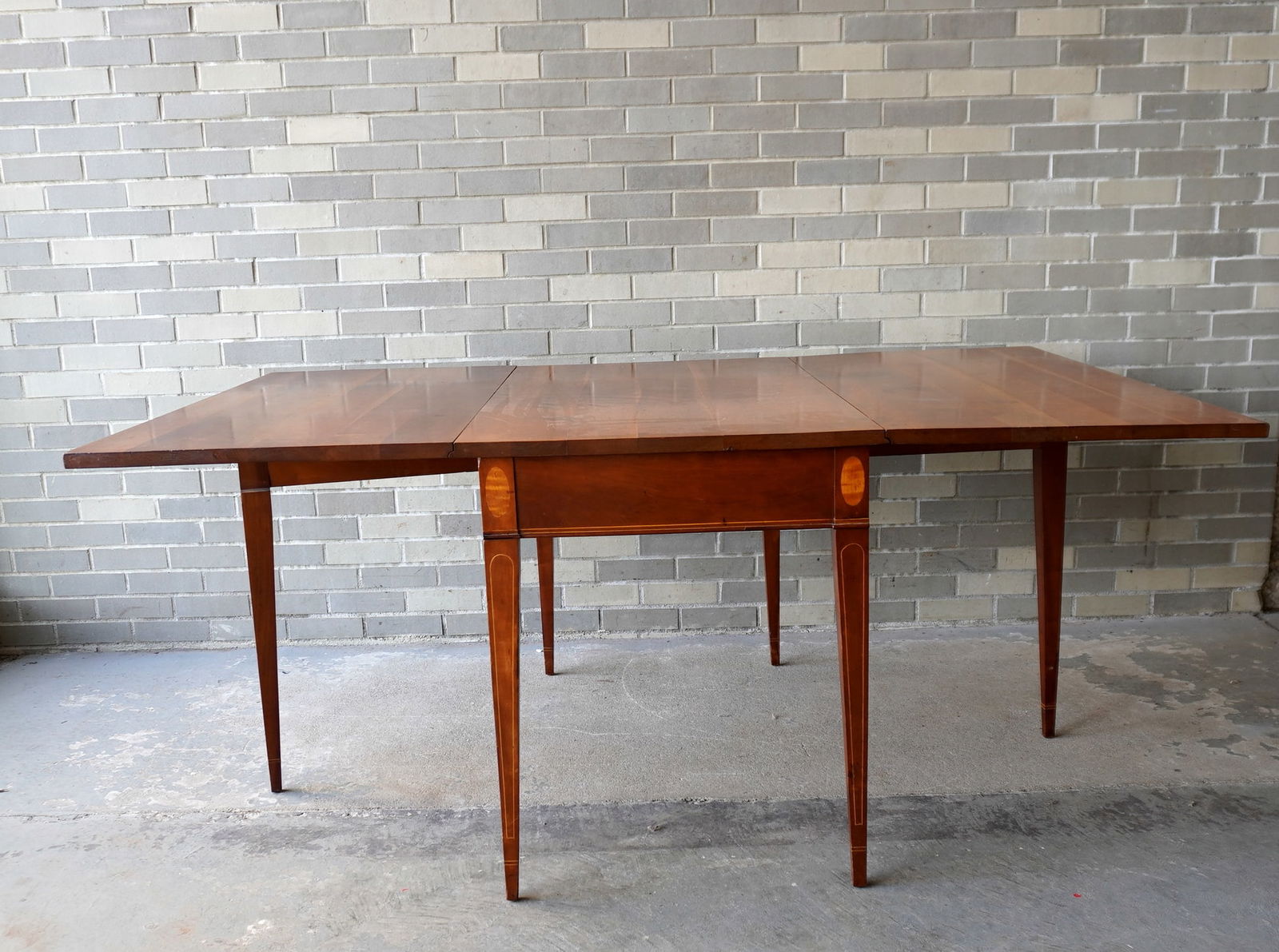 A Hepplewhite style cherry dining room table with long drop leaves and tapered legs - oval inlaid: A Hepplewhite style cherry dining room table with long drop leaves and tapered legs - oval inlaid panels on top of each leg adjacent to apron - the legs and the apron and legs with line inlays. Custom