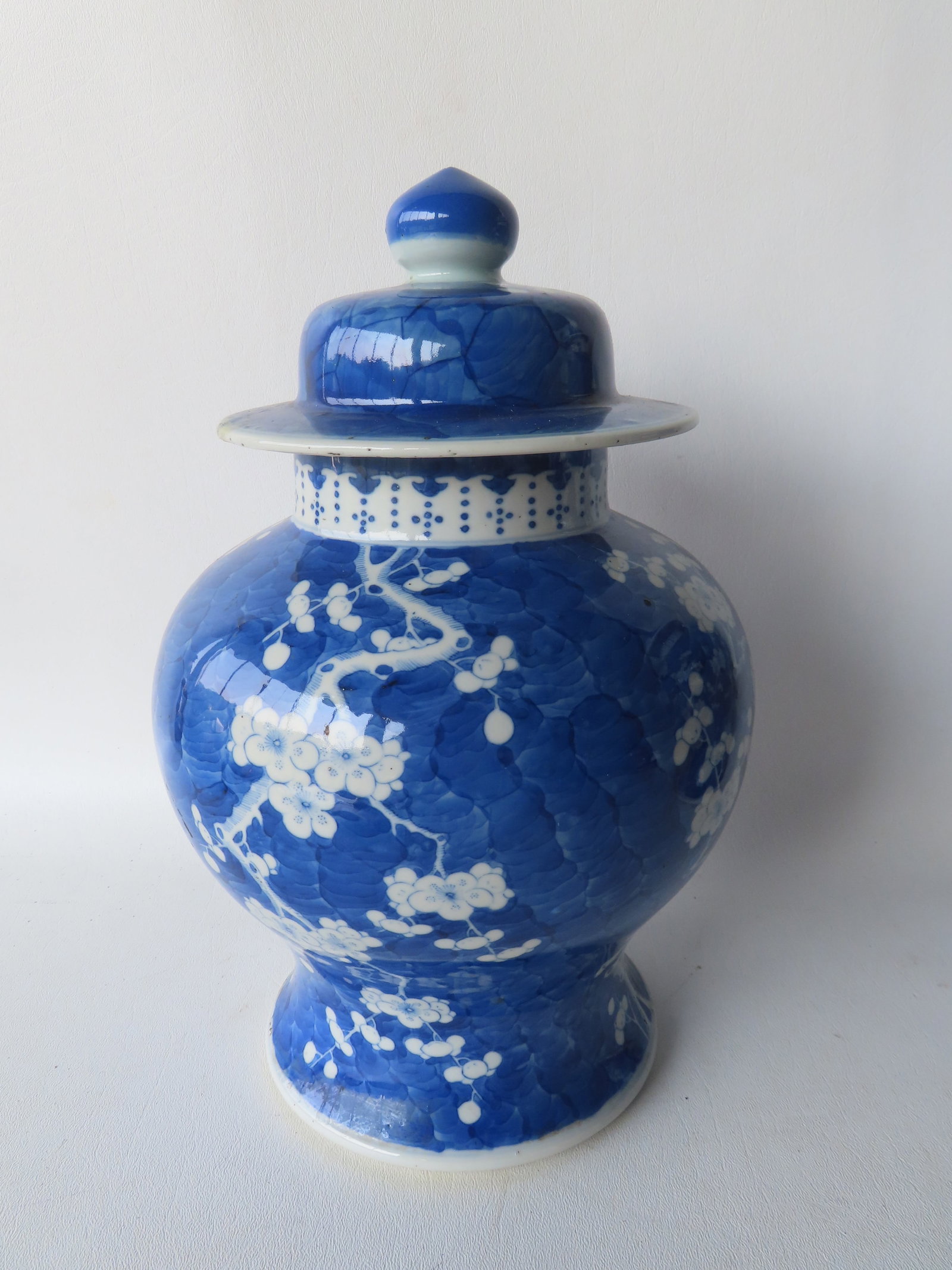 A blue and white ginger jar in classic baluster form, having a domed lid with finial, and decorated: A blue and white ginger jar in classic baluster form, having a domed lid with finial, and decorated with a prunus tree and blossoms (plum tree). It has a double blue circle on the base, indicating lat