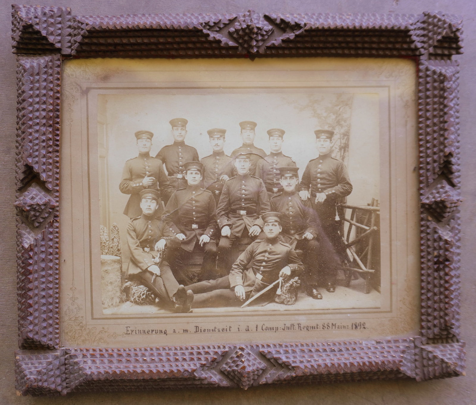 A tramp art frame currently holding a photo of soldiers from Germany, marked "Erinnerung a.m.: A tramp art frame currently holding a photo of soldiers from Germany, marked "Erinnerung a.m. Dienstzeit i. a. l. Comp Juft Regmt. 88 Mainz 1892". The frame with minor edge chips is in good condition 