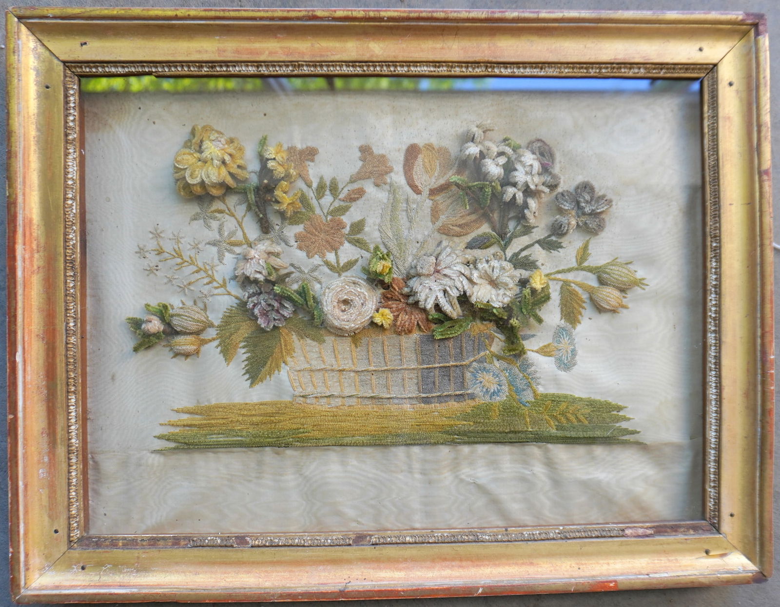 A framed stumpwork embroidery of flowers in a basket, housed in original lemon gold frame, circa: A framed stumpwork embroidery of flowers in a basket, housed in original lemon gold frame, circa 1850. The silk textile background with some foxing, and a small slit on the right side, else good condi
