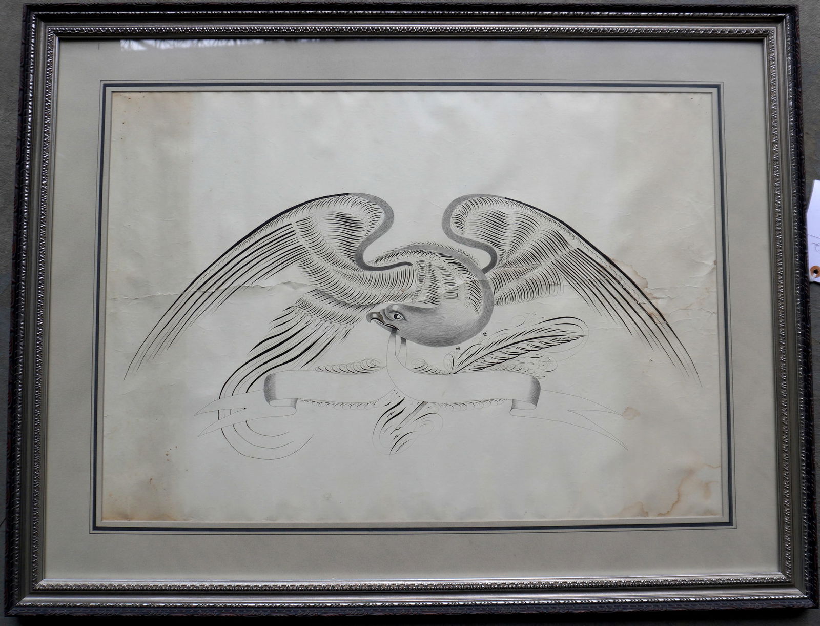 A framed hand drawn pen and ink and graphite calligraphy of a spread wing American eagle holding a: A framed hand drawn pen and ink and graphite calligraphy of a spread wing American eagle holding a banner in beak, circa 1850-70. Some light staining, otherwise very good condition. Total frame size 3