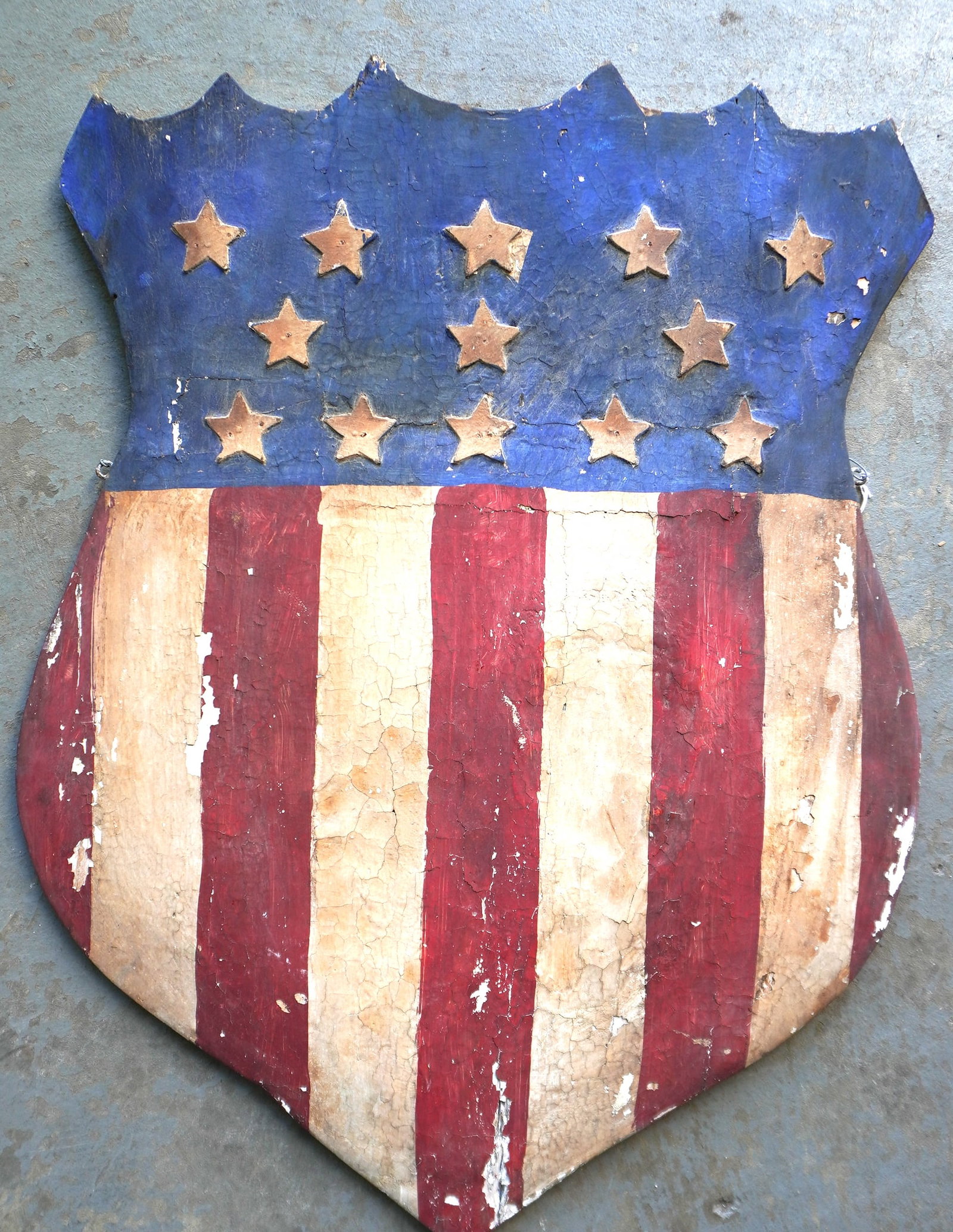 A hand carved wooden American shield with 13 stars, original red, white and blue paint, probably: A hand carved wooden American shield with 13 stars, original red, white and blue paint, probably early 19th century. The stars appear to be applied separately with pin nails. Some wear and losses to p