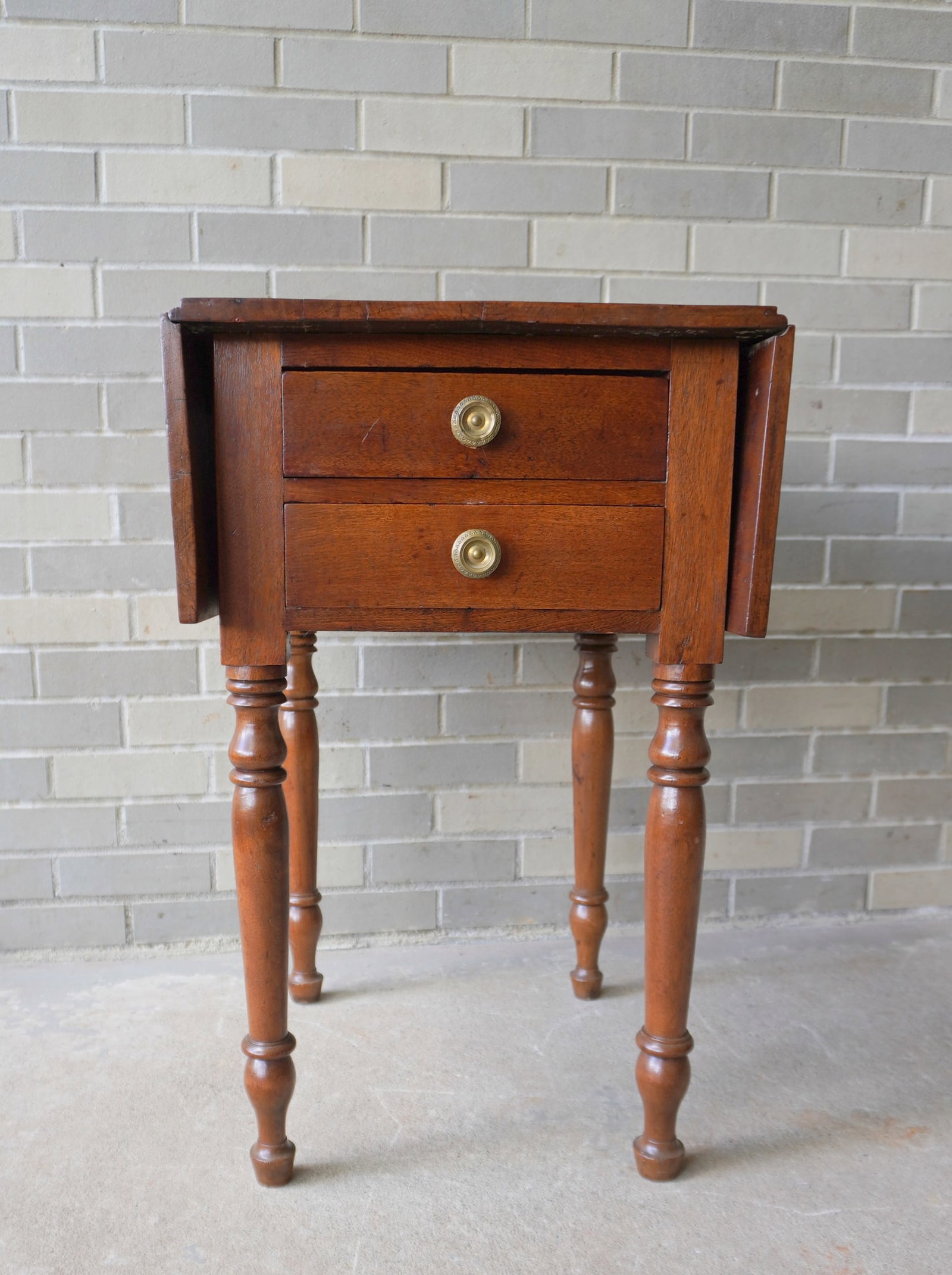 A Sheraton butternut 2 drawer dropleaf sewing stand with original brass pulls, turned legs, and good: A Sheraton butternut 2 drawer dropleaf sewing stand with original brass pulls, turned legs, and good refinished condition, circa 1820. Measures with leaves down 17"W x 22"D and with leaves open 35"W x