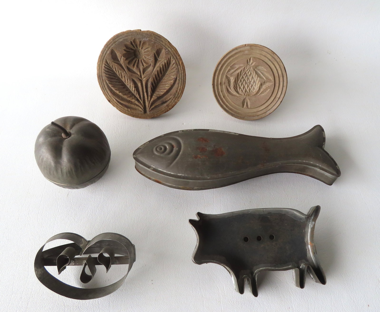 Grouping of 7 early tin and wooden molds, all 19th century, and includes: A tin mold in the form of: Grouping of 7 early tin and wooden molds, all 19th century, and includes: A tin mold in the form of a fish, tin mold in the form of an apple, rare tin cookie mold in the form of a Halloween pumpkin, t