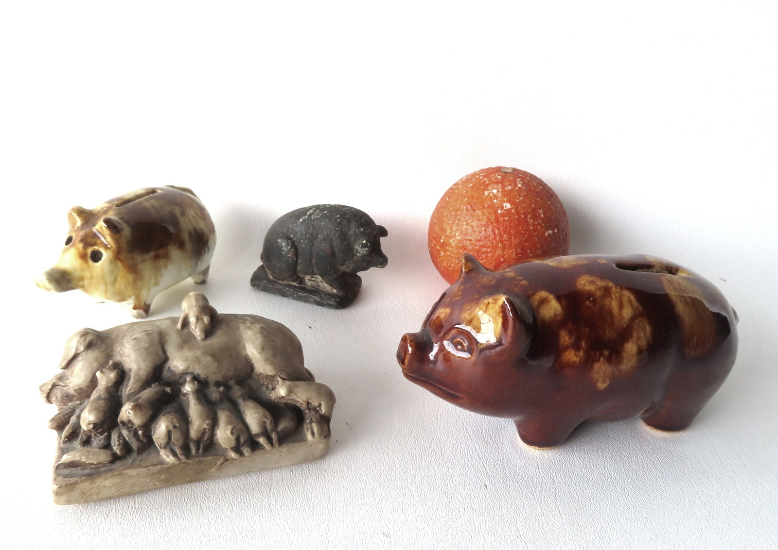 Grouping of 4 pig collectibles including 2 sponge decorated pig form porcelain banks, a small cast: Grouping of 4 pig collectibles including 2 sponge decorated pig form porcelain banks, a small cast iron pig paperweight, and a sculptured stone or composition pig with piglets & corn paperweight - tra