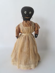 A folk art black bottle doll made from a black stocking having metal circular earrings, eyes appear