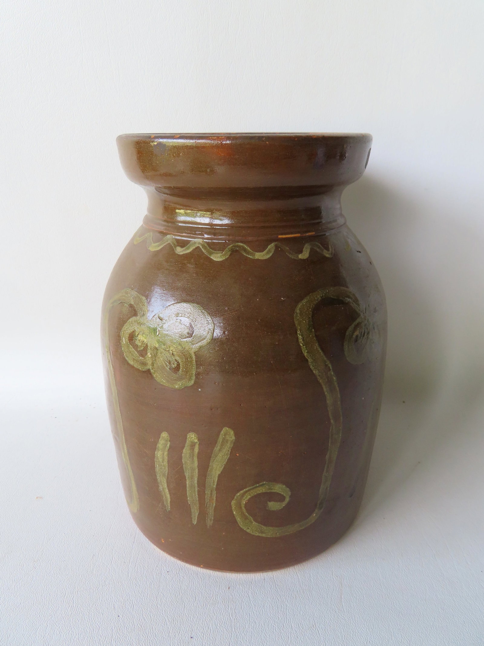 A stoneware jar with Albany glaze and decorated wish a lighter brown slip in the form of stylized: A stoneware jar with Albany glaze and decorated wish a lighter brown slip in the form of stylized flowers and grass and having squiggle decorations around the base of the flared neck. Several small ch