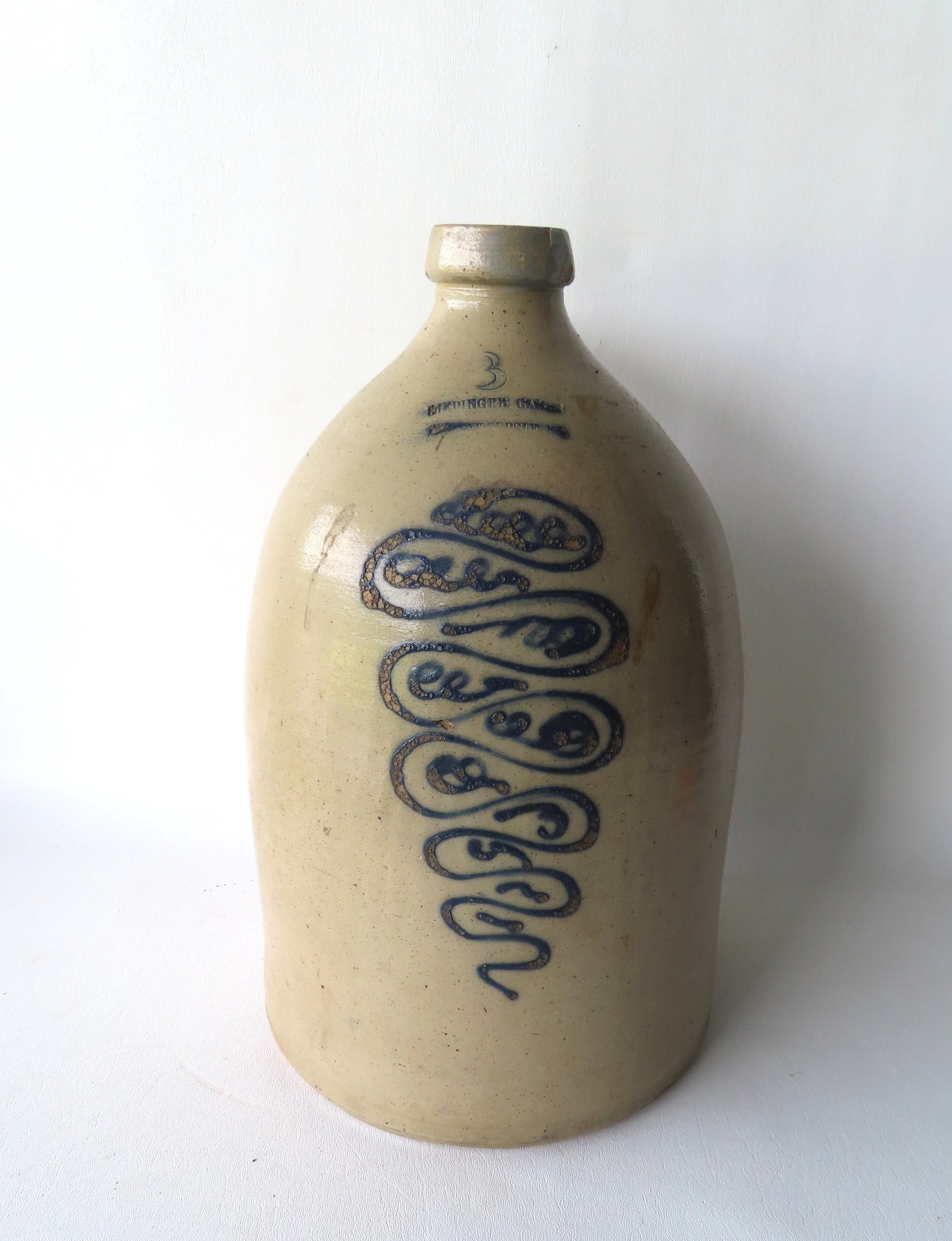 A stoneware jug decorated with a cobalt blue tornado design, with the impressed mark of "RIEDINGER: A stoneware jug decorated with a cobalt blue tornado design, with the impressed mark of "RIEDINGER CAIRE / POUGHKEEPSIE NY", 3 GALLON SIZE. Measures 16"H x 9"W. Rim chip with repair, else good conditi
