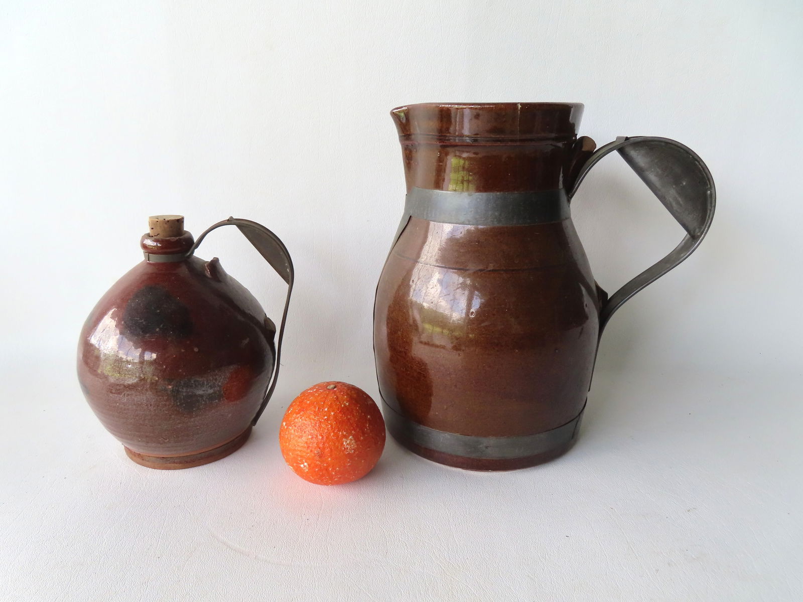 Two redware & stoneware pitchers with replaced make-do handles taken for 19th tinware. The first, an: Two redware & stoneware pitchers with replaced make-do handles taken for 19th tinware. The first, an ovoid redware pitcher with manganese decorations - 7"H x 6 1/4"W - early to mid 19th century; the s