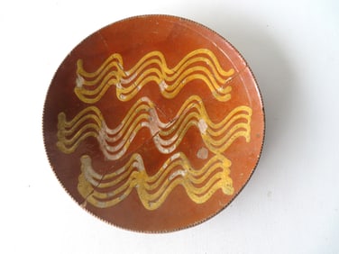 A redware plate with yellow slip squiggles and coggled edges - broken and repaired - some losses to