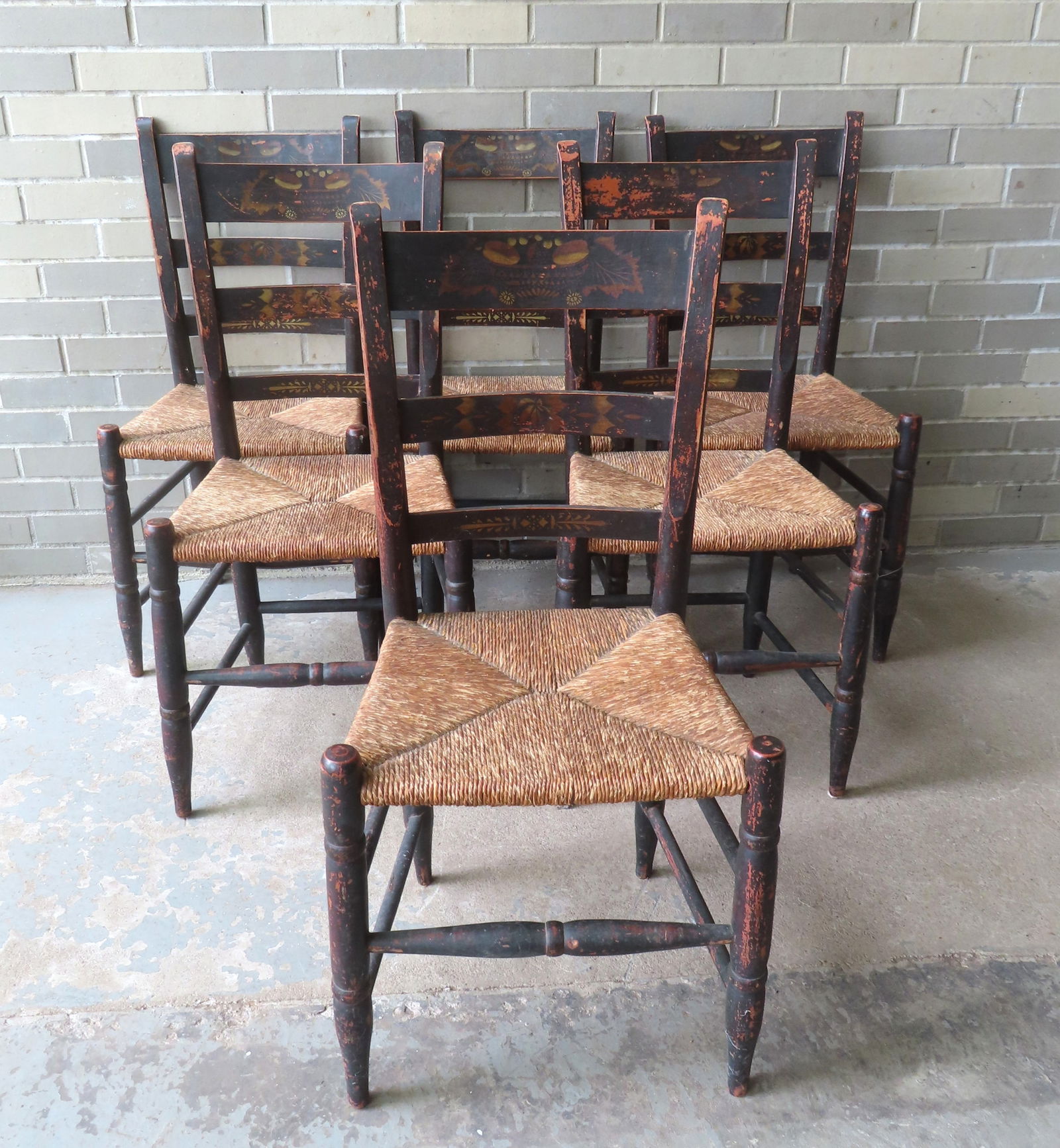 A set of 6 country rabbit ear country chairs in original paint with a back splat stencil decorated: A set of 6 country rabbit ear country chairs in original paint with a back splat stencil decorated with a basket of fruit and leaves, all with rush seat. One chair with wear to back, the others all in