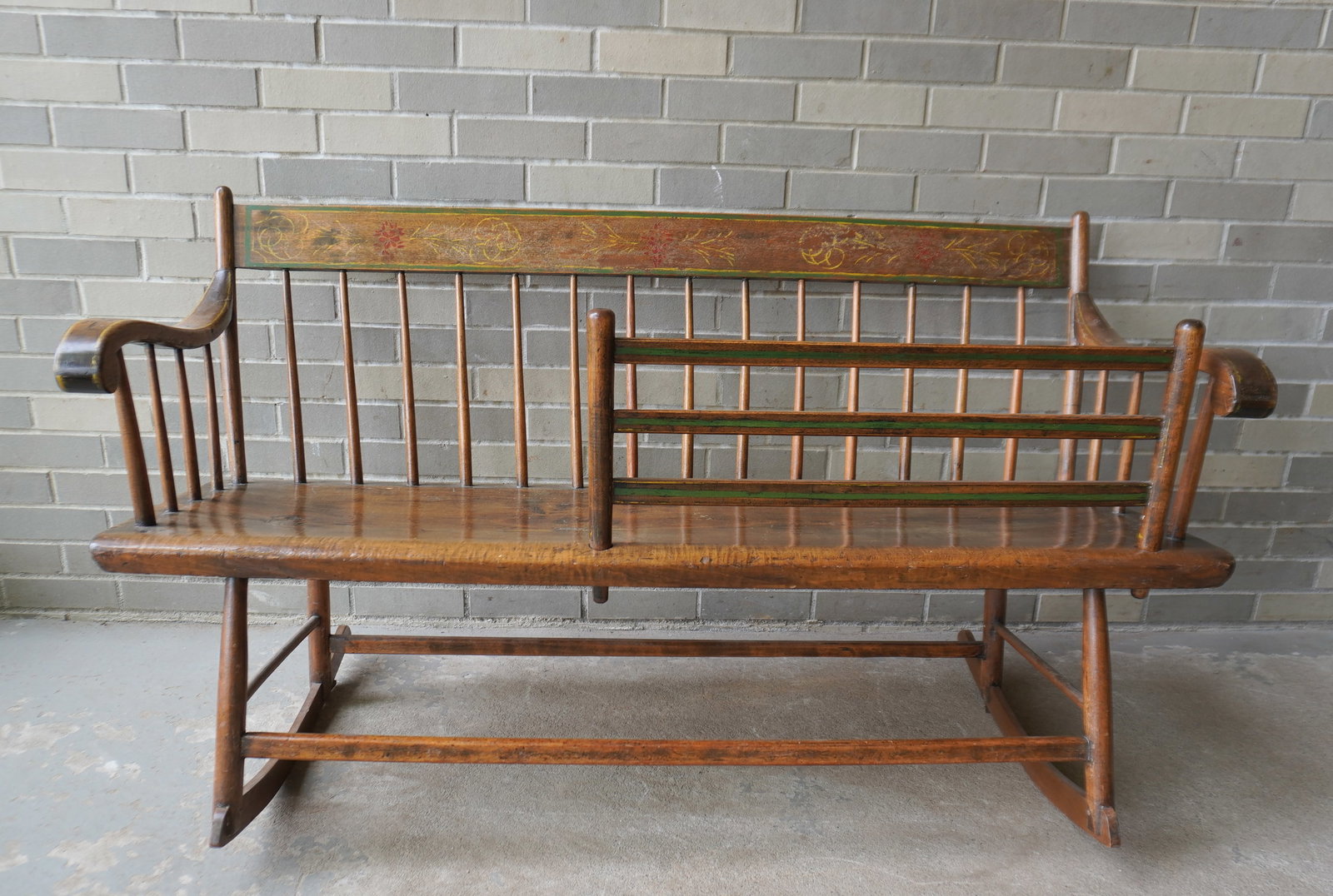 A Windsor mammy's rocking bench with removable child guard. One board saddle seat. Appears to retain: A Windsor mammy's rocking bench with removable child guard. One board saddle seat. Appears to retain original stenciling which is worn, otherwise good condition. Measures 53"W x 24"D x 33"H.