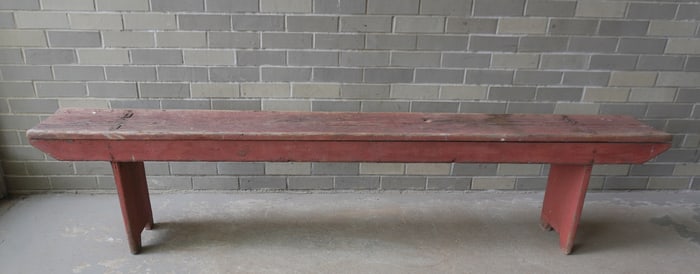 A very primitive country bench in original red paint, mortised through legs with shaped terminal -
