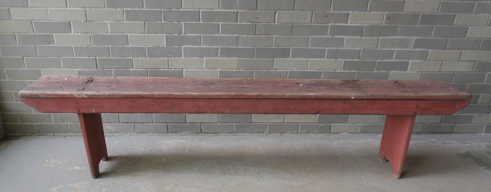 A very primitive country bench in original red paint, mortised through legs with shaped terminal -: A very primitive country bench in original red paint, mortised through legs with shaped terminal - weathered with slight wobble, fair good condition, early 19th century. Measures 84 1/4"L x 12"D x 18"