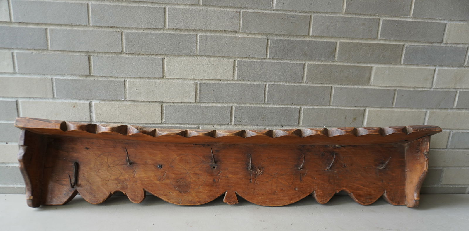An early wall hanging wooden shelf/game rack with hand forged iron hooks, and scalloped edge on: An early wall hanging wooden shelf/game rack with hand forged iron hooks, and scalloped edge on shelf edge and apron, 18th century. Measures 45"W x 6 1/2"D x 9"H