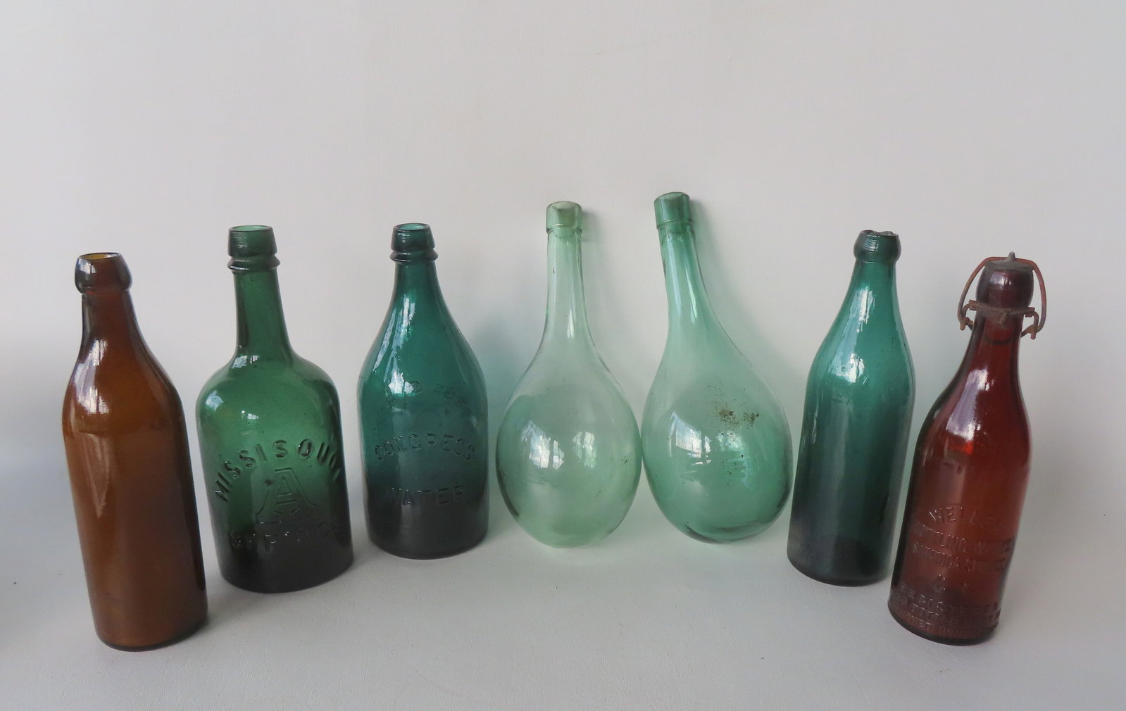 Grouping of 7 water and soda bottles including "Missisquoi A Springs" in green - 9 3/4"H; marked: Grouping of 7 water and soda bottles including "Missisquoi A Springs" in green - 9 3/4"H; marked "Congress Spring Co. / C / Saratoga N.Y." on one side and "Congress Water" on the other side, whittled 