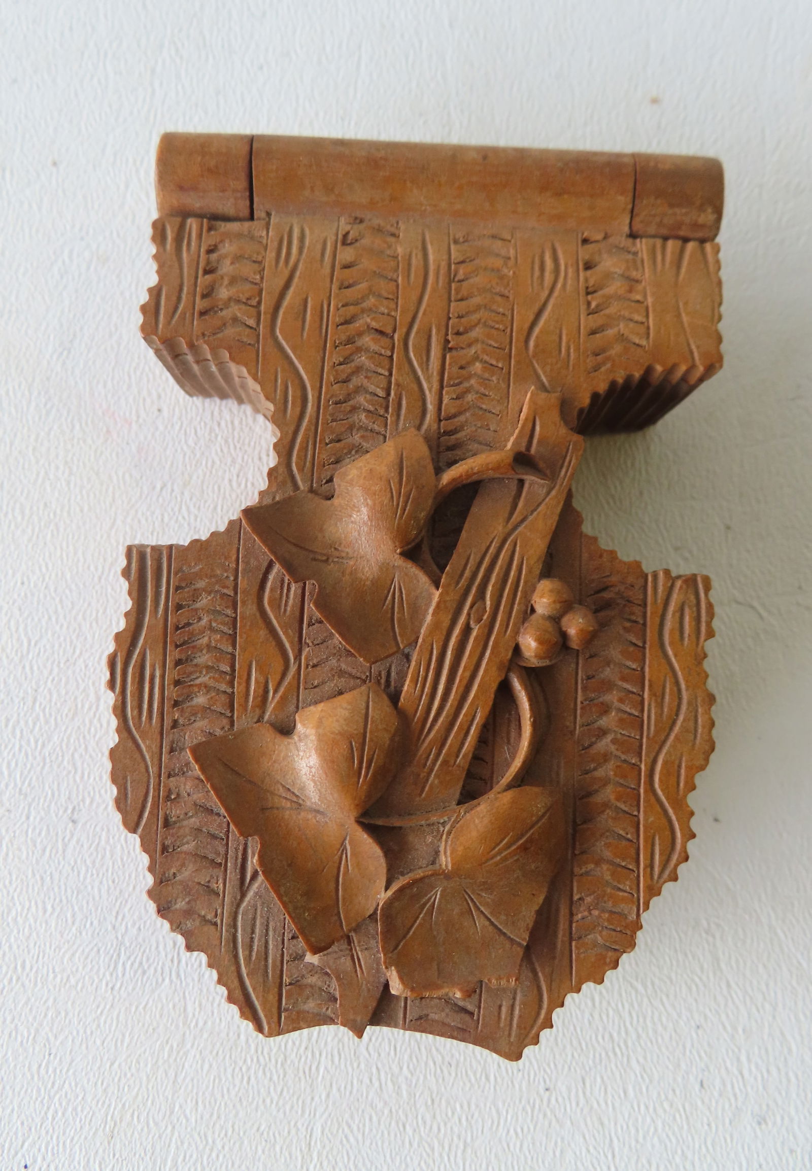 A carved wood pocket watch holder and display, with leaves and berries relief carved on folding lid,: A carved wood pocket watch holder and display, with leaves and berries relief carved on folding lid, probably Black Forest Germany, 19th century. Measures 4"H x 2 1/2"W. Provenance: From a Rochester N