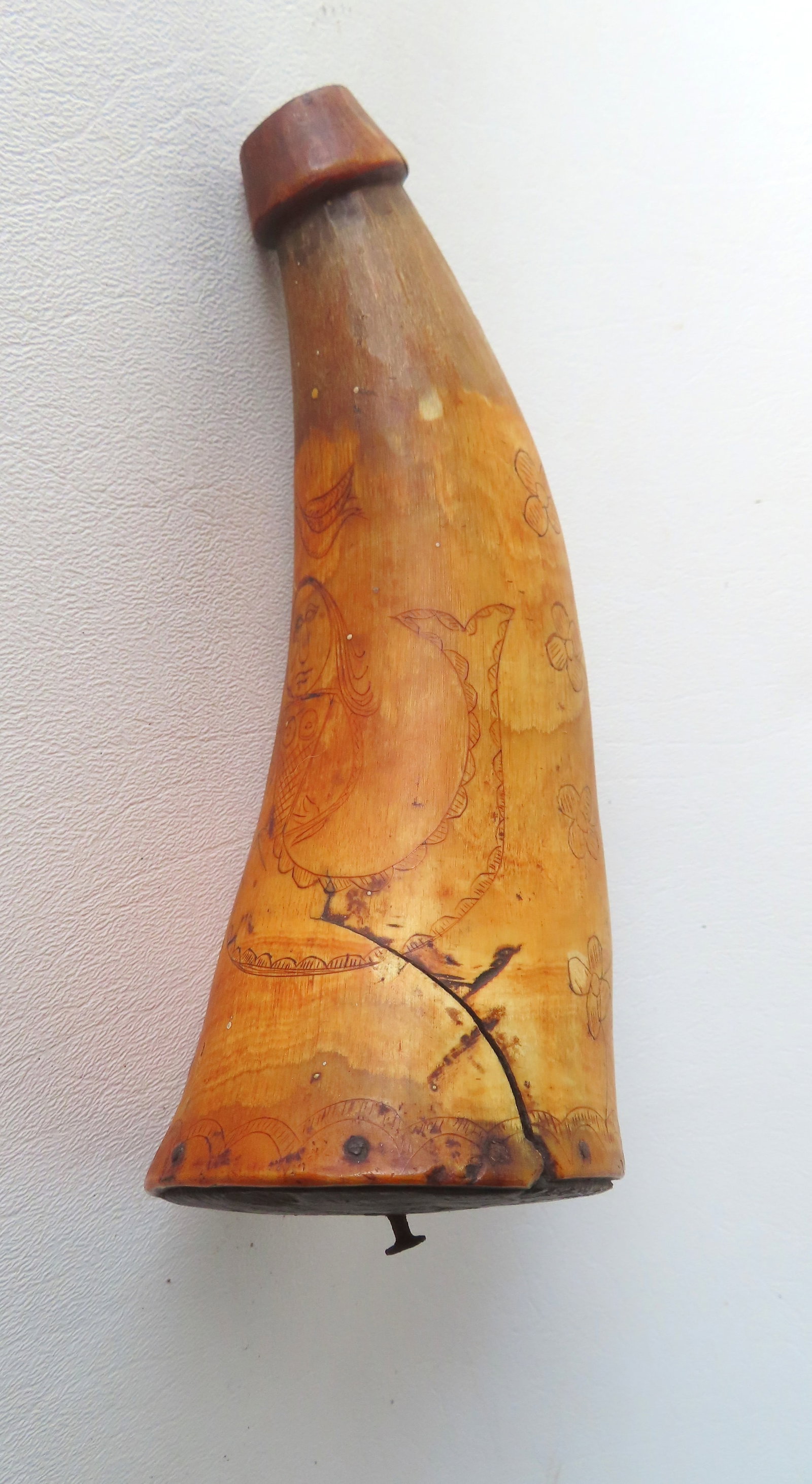 A folk art powder horn with scrimshaw of 2 birds flying above 2 mermaids separated by flowers, 18th: A folk art powder horn with scrimshaw of 2 birds flying above 2 mermaids separated by flowers, 18th century. Original wood base plate marked with maker's initials "B A". Irregular crack extending from