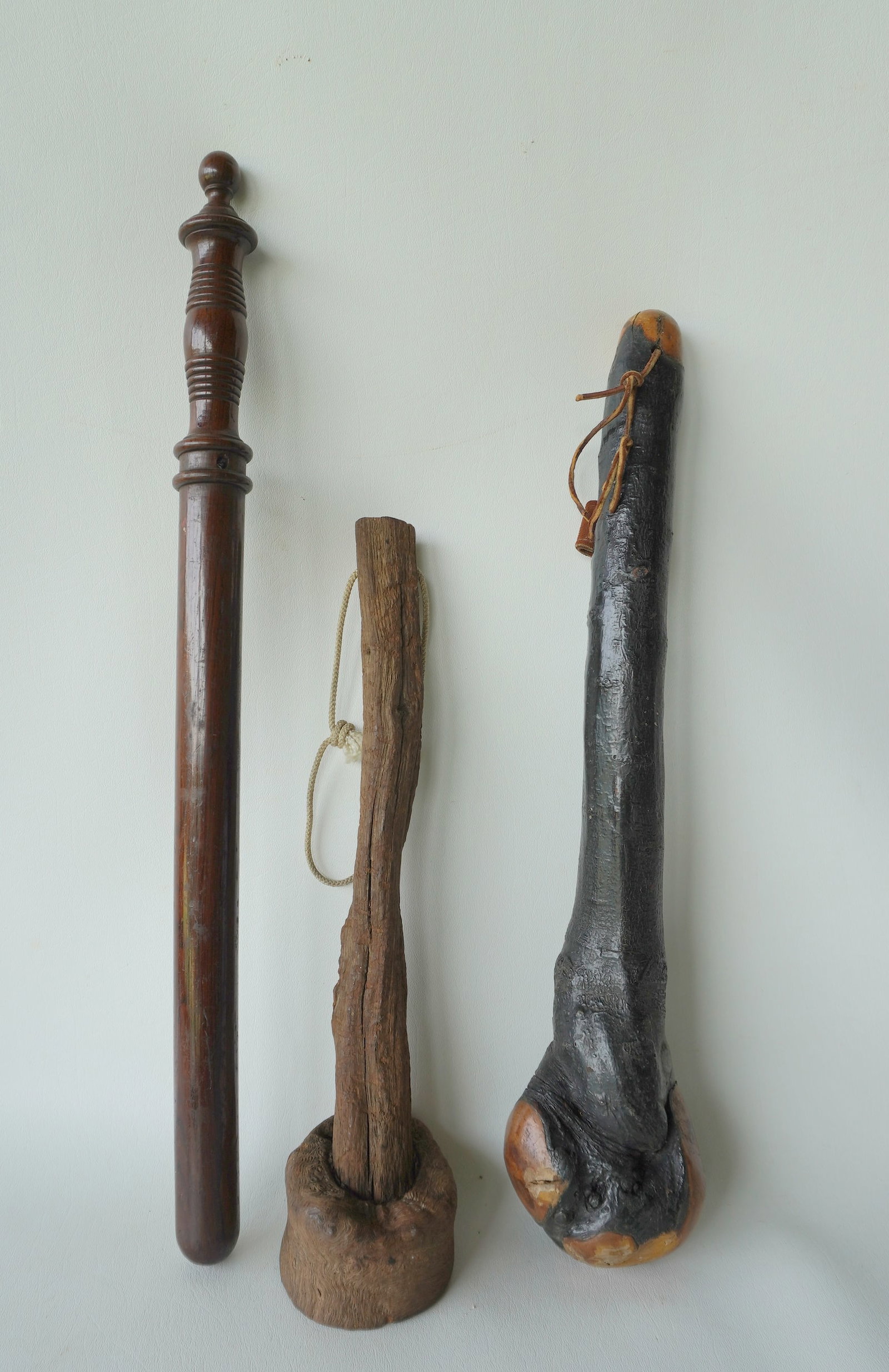 Three vintage wooden clubs, all 19th century and in very good condition, including: A primitive: Three vintage wooden clubs, all 19th century and in very good condition, including: A primitive natural burlwood club or pestle; a refined rosewood policeman's night stick with turned handle; and a na