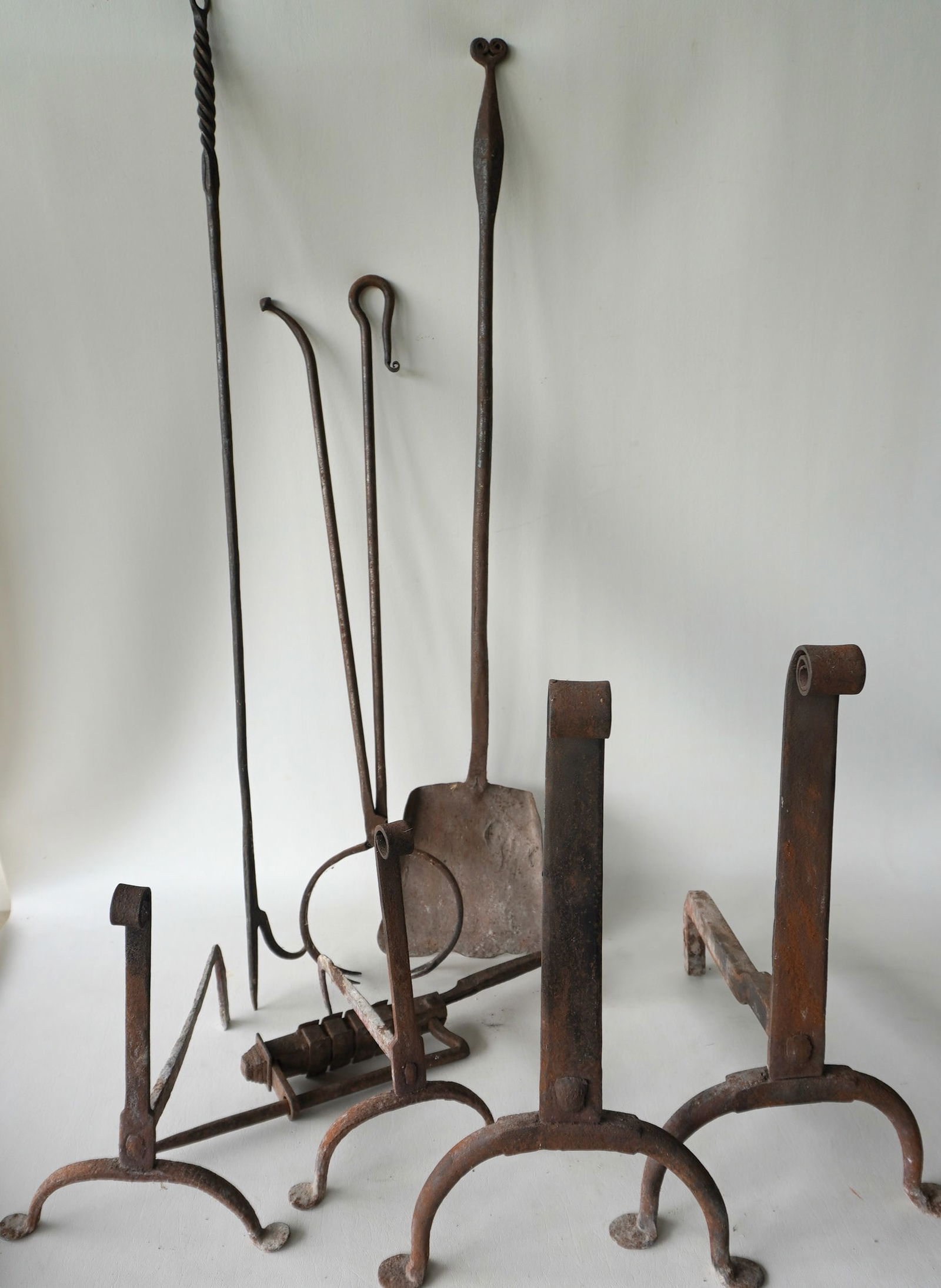 Grouping of early iron, mostly hearth related, including: Two pair of hand forged andirons with: Grouping of early iron, mostly hearth related, including: Two pair of hand forged andirons with penny feet, early 18th century - the largest of the 2 measures 17 1/2"H x 16"D x 11"W; long handled shov