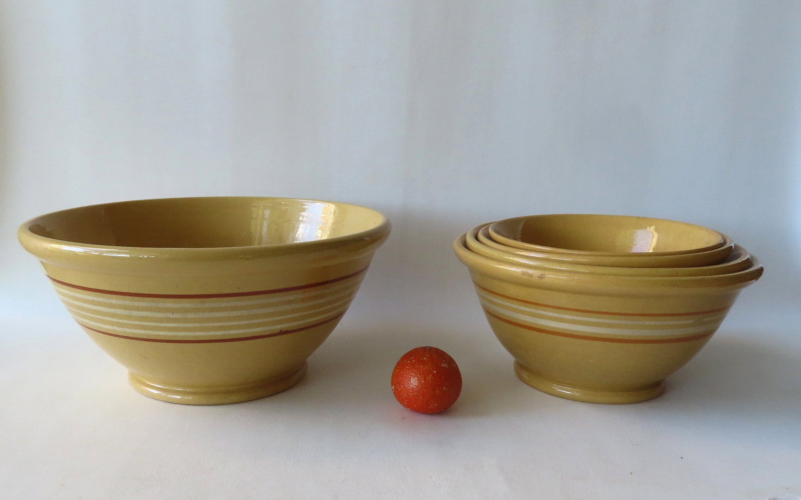 Grouping of 5 yellowware mixing bowls with rolled rims and footed bases. Includes a matching nested: Grouping of 5 yellowware mixing bowls with rolled rims and footed bases. Includes a matching nested set of 4 with a brown ring separating 2 white rings - ranging in size from 10 1/4" diameter x 4 1/2"