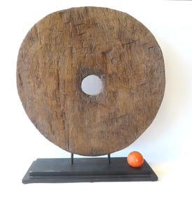 An ancient hand chiseled primitive cart wheel, mounted on a museum stand for display purposes.