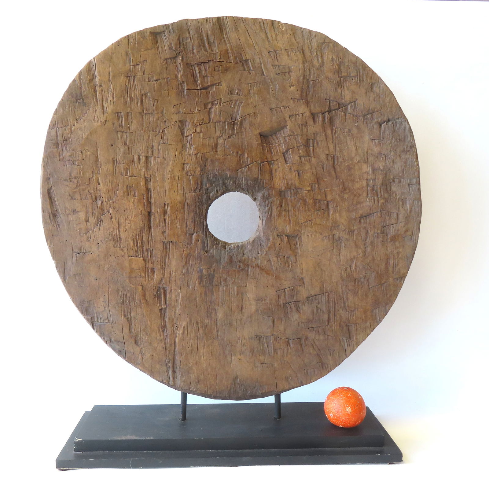 An ancient hand chiseled primitive cart wheel, mounted on a museum stand for display purposes.: An ancient hand chiseled primitive cart wheel, mounted on a museum stand for display purposes. Measures 27" diameter (slightly out of round) x 1 3/4" thick. Unknown origin. Provenance: From the Marni