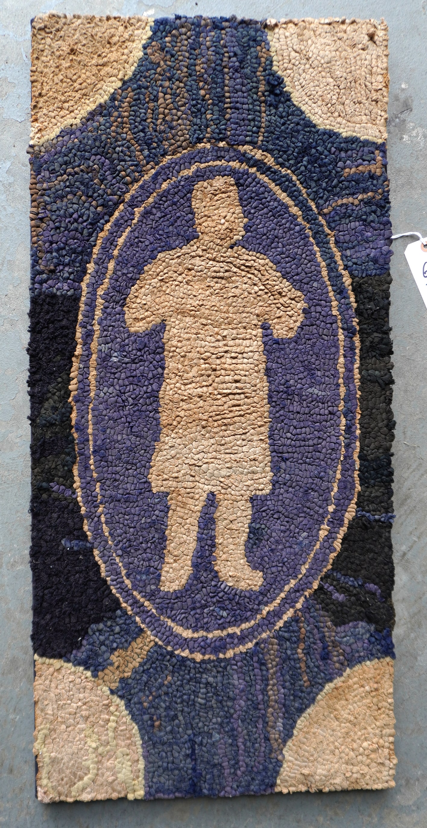 A folk art mounted hooked rug having fan shaped corners, striated background and a central figure of: A folk art mounted hooked rug having fan shaped corners, striated background and a central figure of what appears to be a person wearing hat, long coat and boots holding an article (or animal) in his/