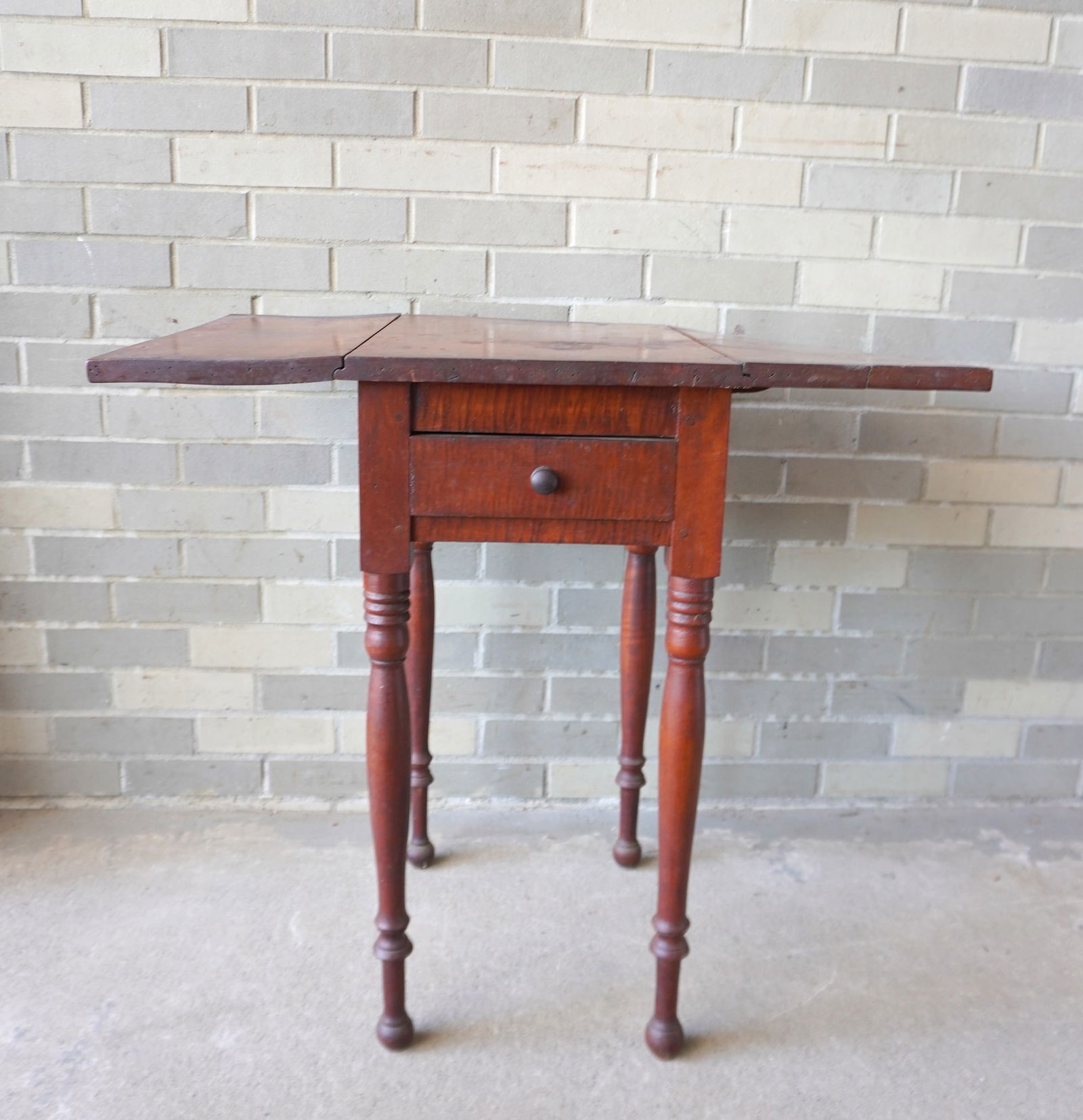 A Sheraton tiger maple 1 drawer drop leaf sewing stand on turned legs, circa 1820. One leaf slightly: A Sheraton tiger maple 1 drawer drop leaf sewing stand on turned legs, circa 1820. One leaf slightly warped, else good original condition. Measures 15"W x 20"D x 29"H