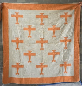 A folk art Charles Lindbergh airplane quilt decorated with orange images of the Spirit of St. Louis,