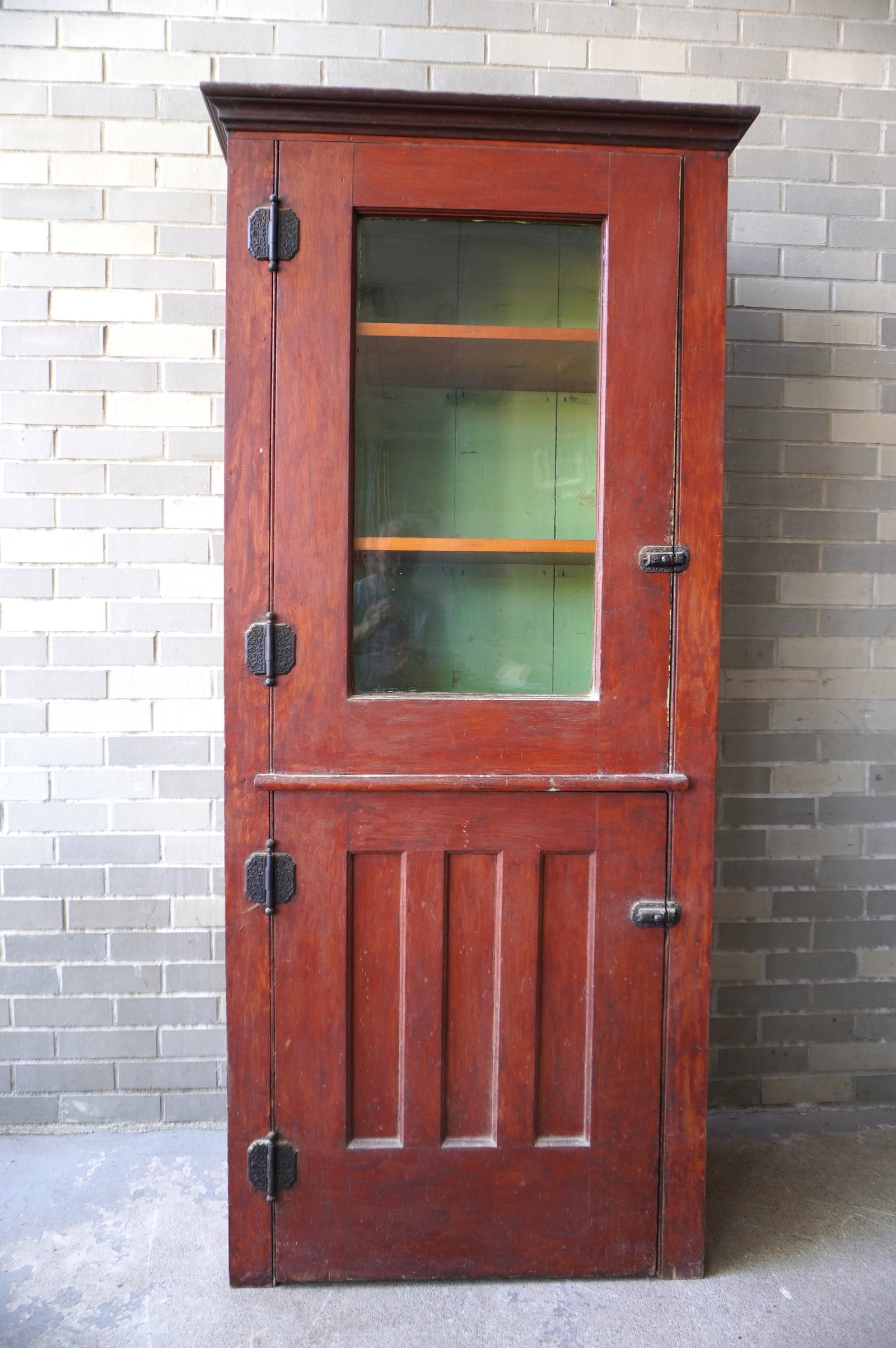 A primitive pine cupboard in original red stain, single glass door over a paneled door and having a: A primitive pine cupboard in original red stain, single glass door over a paneled door and having a molded cornice. Very good condition. Circa 1875. Measures 32 3/4"W x 15 1/2"D x 72 1/4"H. Provenance
