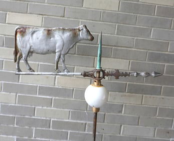 A lightening rod with painted tin cow mounted on arrow directional over milk glass ball. No roof