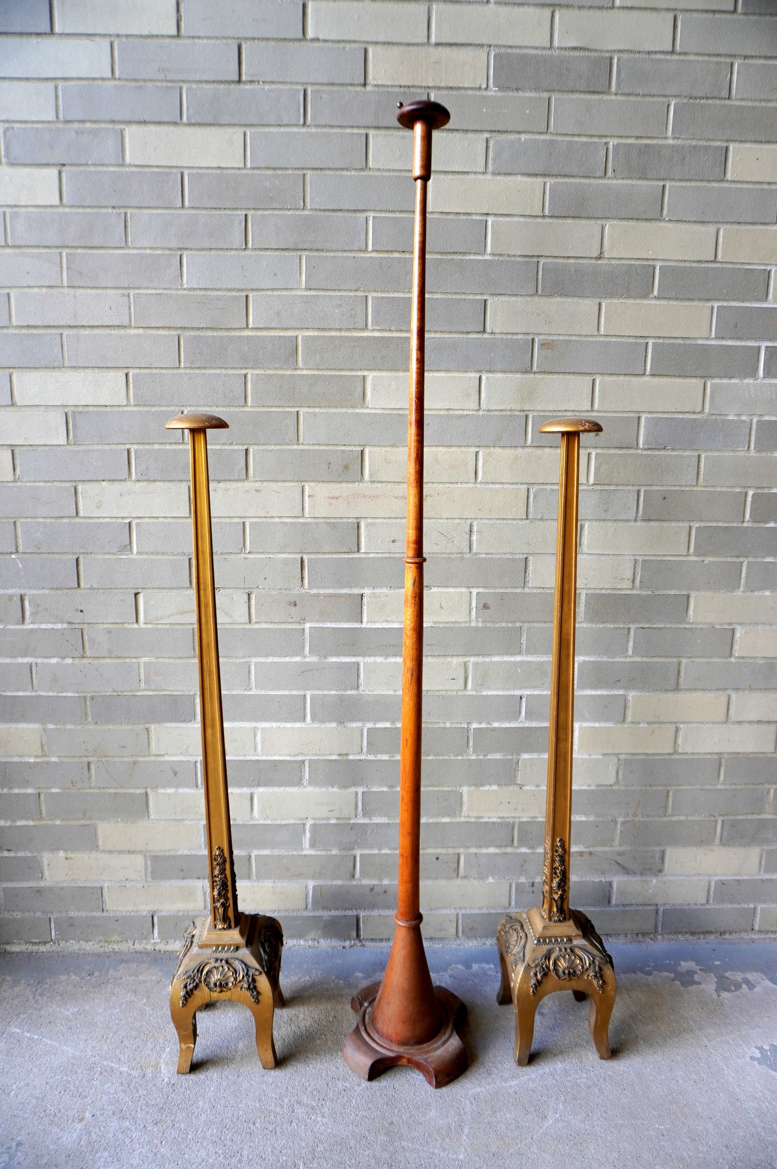 Three carved wooden floor standing bonnet holders including: Two matching gilded wooden stands in: Three carved wooden floor standing bonnet holders including: Two matching gilded wooden stands in the French style mounted on 4 short cabriole legs and with ornate bases with applied gesso ornaments, 